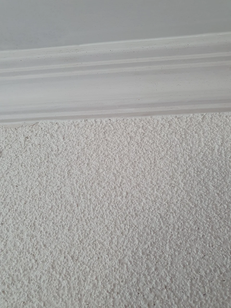 Detail eines weissen Stuckprofils ĂĽber einer strukturierten Wand
