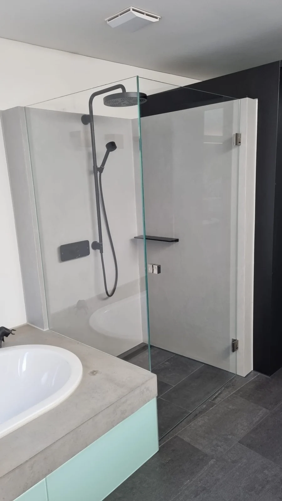 Dusche mit hellen fugenlosen Wandflächen und Glasabtrennung